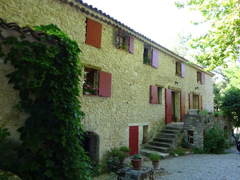Stone farmhouse with red shutters, ivy and outdoor steps among trees