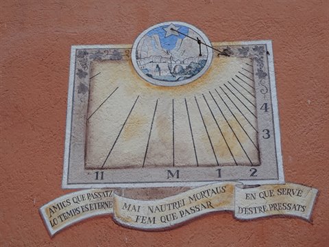 Painted sundial on ochre wall with Catalan inscriptions and mountain scene
