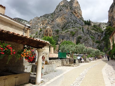 Moustiers-Sainte-Marie: woman by stone fountain under flowered pergola