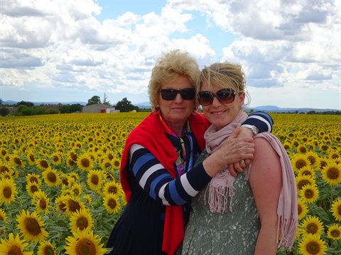 Two women in sunglasses embracing in a blooming sunflower field