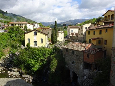Stone village with yellow houses above a stream, Tuscan hills under clouds