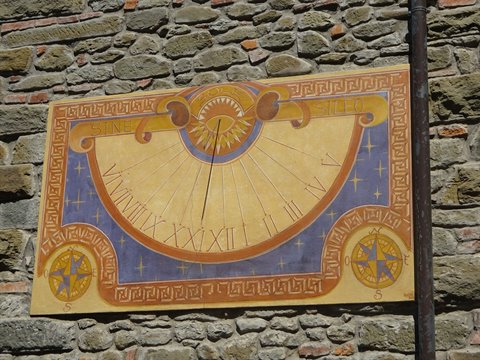 Painted sundial in ochre and blue on a stone wall, sunlit