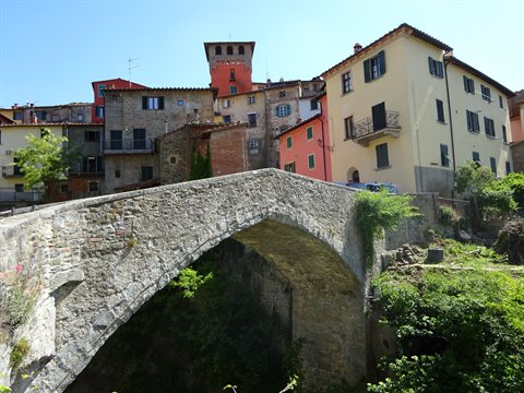 Medieval stone bridge in Loro Ciuffenna, colorful houses under sunny sky