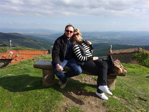 Couple sitting on stone bench above red-tiled rooftops, green hills