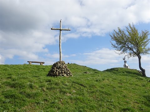 Wooden cross on stone pile, green meadow, bench and tree
