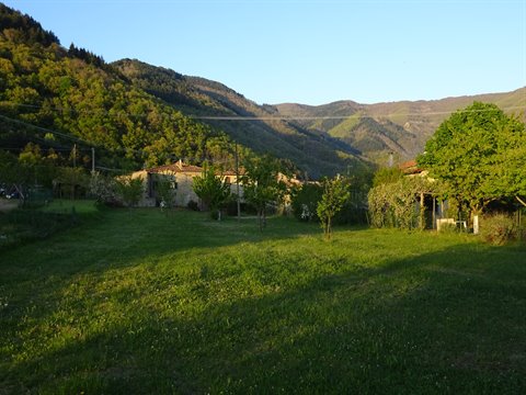 Green meadow before stone farmhouses among wooded hills, golden light