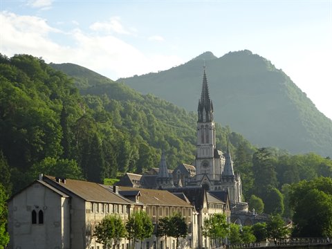 The basilica of Lourdes stands among green trees and mountains