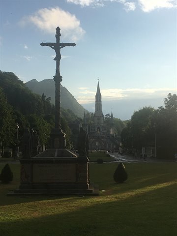 Stone crucifix in front of Lourdes basilica, morning light on the lawn