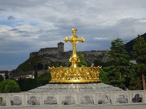 Golden crown with cross atop the Lourdes basilica, castle on the hill