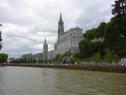 Gothic stone basilica above the river in Lourdes, pilgrims along the bank