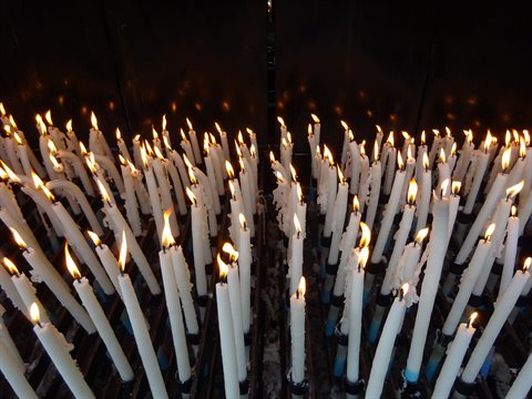 White votive candles burning in a church, flames glowing in darkness
