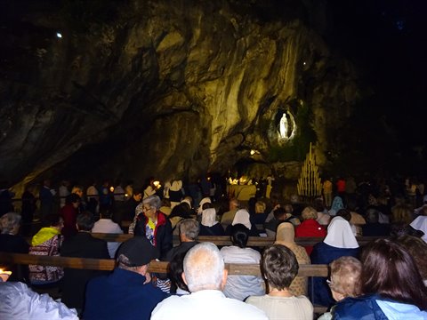 Pilgrims praying at the Massabielle Grotto in Lourdes, lit at night
