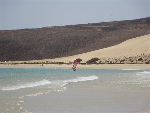 Windsurfer with red sail on golden sandy beach and dunes