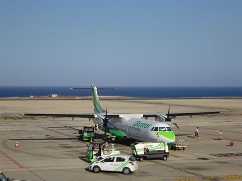 Binter turboprop aircraft parked on airport apron with service vehicles nearby