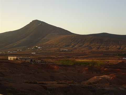 Brown volcanic mountain and scattered white houses in golden evening light