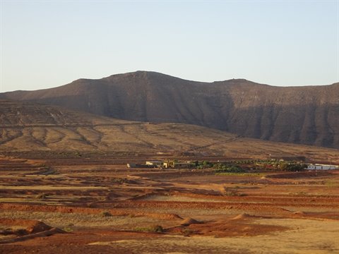 Low houses and reddish dry fields at the foot of volcanic mountains