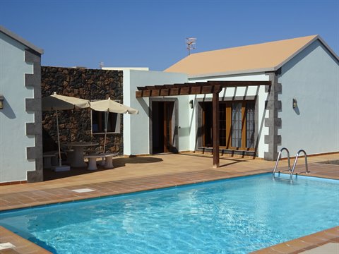 White house with wooden pergola and blue pool under sunny sky