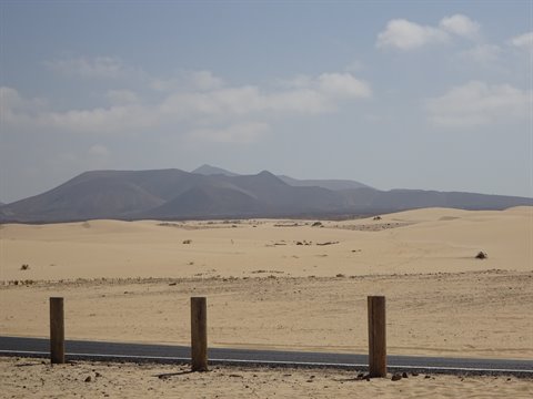 Golden sand dunes beside the road, volcanic mountains in the background