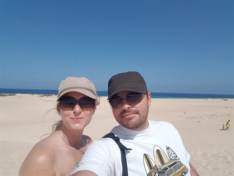 Couple selfie in hats and sunglasses on sandy dunes facing the blue sea
