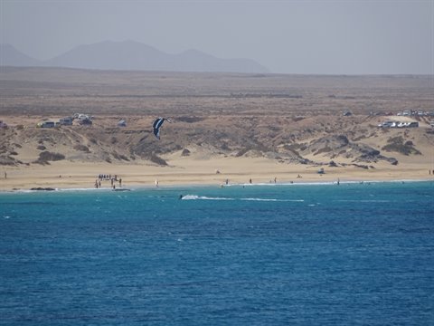 Kitesurfer on turquoise water in front of sandy beach and desert dunes