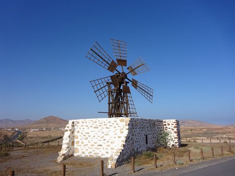 Traditional stone windmill with wooden blades under blue sky
