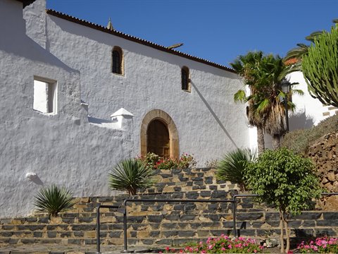 White church with arched doorway, stone staircase and palm trees under blue sky