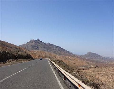 Asphalt road with guardrail through arid mountains under blue sky, Fuerteventura