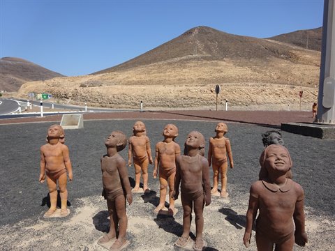 Bronze statues of children gazing skyward beside a desert road