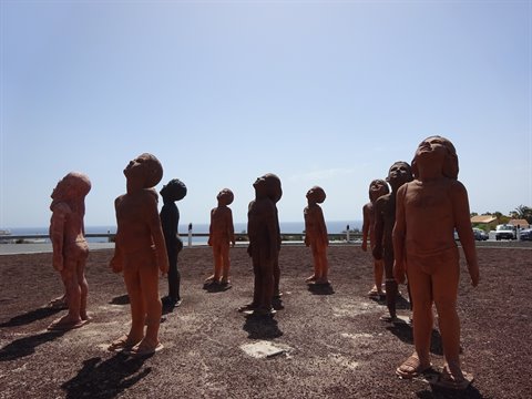 Terracotta statues of children gaze upward by the seaside