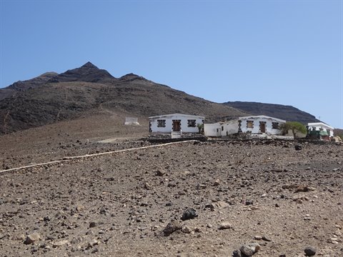 White stone houses on arid volcanic terrain beneath mountains, clear blue sky