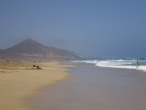 Golden sand beach with waves and volcanic cone in the background