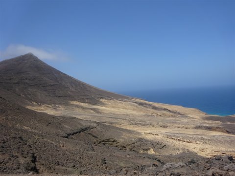 Arid volcanic mountain slopes down to the coast, blue ocean and clear sky