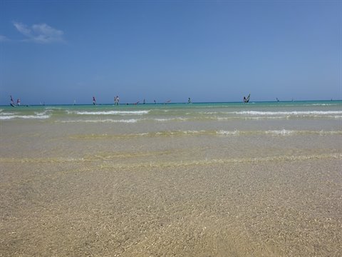 Windsurfers on turquoise water in front of pale sandy beach