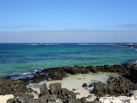 Turquoise water between black lava rocks and white sand, blue sky