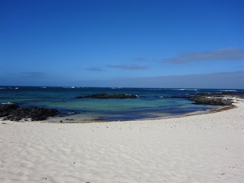 White sand beach with black rocks and turquoise water under blue sky