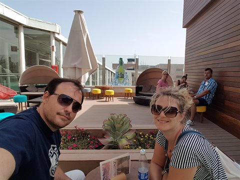 Couple in sunglasses selfie on wooden rooftop terrace with umbrella and round sofas