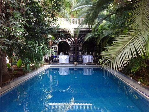 Piscina azzurra tra palme e tavole apparecchiate nel riad a Marrakech