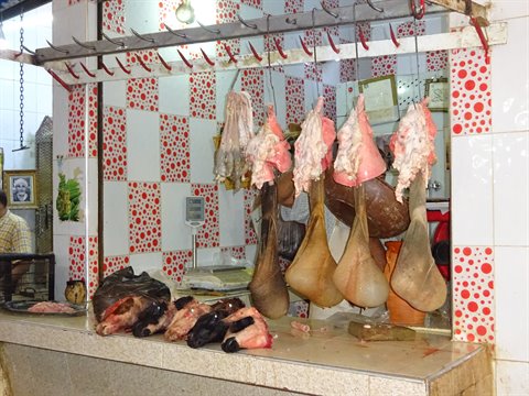 Macelleria con carne appesa all'uncino tra piastrelle rosse a Fes