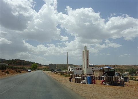 White minaret beside the road, fuel bottles for sale, cloudy sky