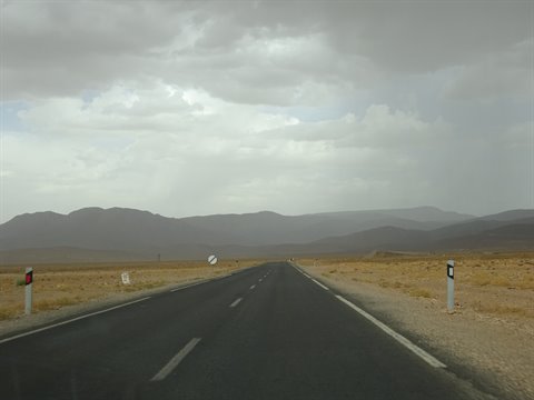 Asphalt road toward Errachidia across arid steppe and mountains under grey clouds