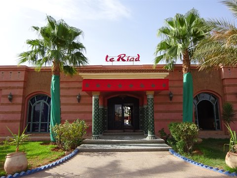 Entrance of Le Riad, pink facade with palm trees and green columns