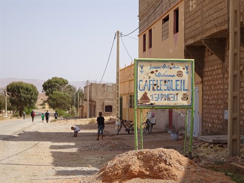 Café Le Soleil sign along a village dirt road, children and bicycles