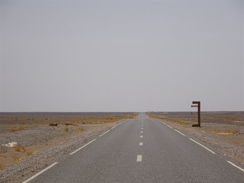 Strada dritta d'asfalto nel deserto pietroso, vecchio cartello arrugginito