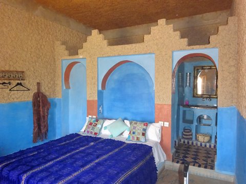 Camera con archi dipinti di azzurro, letto coperto di blu e bagno affrescato