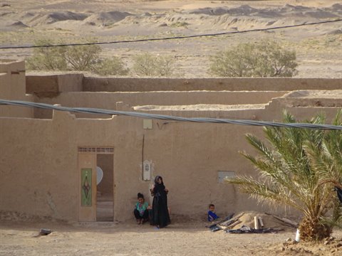 Donna in nero con due bambini davanti a casa di terra, Merzouga