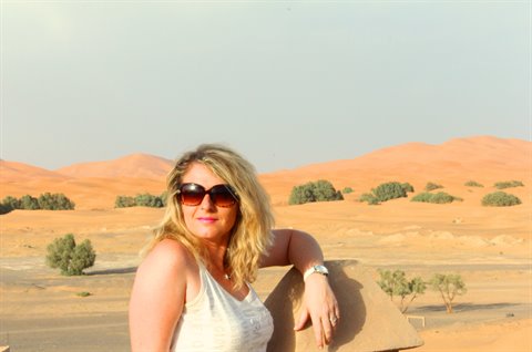 Donna bionda con occhiali da sole appoggiata alle dune di Merzouga