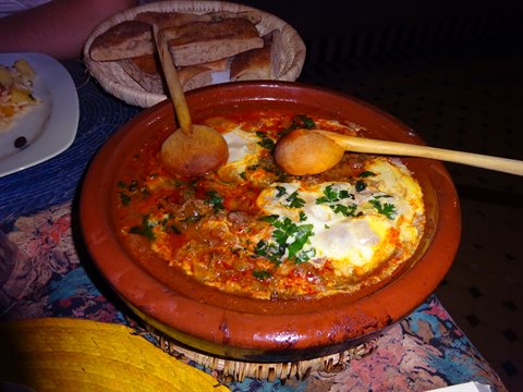 Tagine in terracotta con uova e prezzemolo, cesto di pane accanto