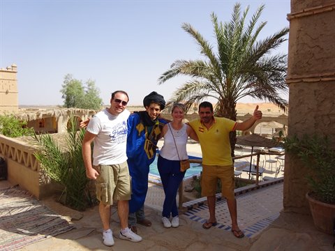 Tourists with guide in traditional dress among palms and earthen terraces in Merzouga