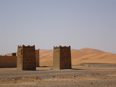 Mud-brick gate towers before the sand dunes of Merzouga