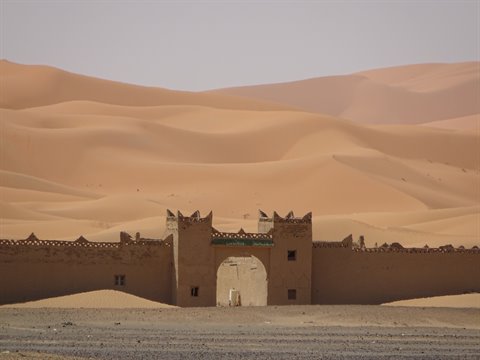 Mud-brick gateway standing before the sand dunes of Merzouga
